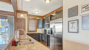 A kitchen with granite countertops, stainless steel appliances, wooden beams, and a large refrigerator.