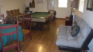 Un salon comprenant une table de billard, un canapé et un coin repas avec des chaises.