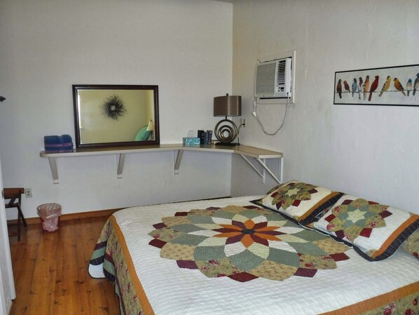 A bedroom with a bed, a desk, a chair, a wall-mounted air conditioner, a framed picture, and a wall art of birds.