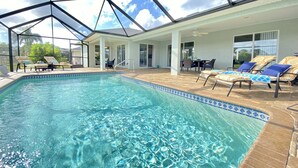 A swimming pool with clear blue water, surrounded by lounge chairs and a covered patio area.