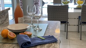 A dining area with a table set for two, featuring a bottle of wine, wine glasses, plates, cut oranges, a knife, and a blue napkin.