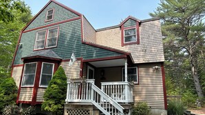 A two-story house with a front porch, a staircase, and a flag. - Tall pines & lake view. Perfect location ctr of MDI! Close trails.  Local owners (Mt Desert)