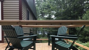 A wooden deck with two Adirondack chairs and a small table, overlooking a forested area. - Tall pines & lake view. Perfect location ctr of MDI! Close trails.  Local owners (Mt Desert)