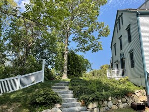 Eine Steintreppe führt zu einem Haus mit weißem Zaun und einem großen Baum im Vordergrund.