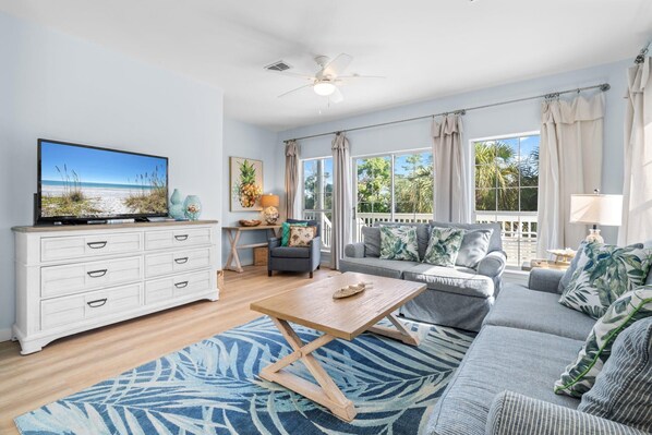 A living room with a TV, sofa, coffee table, and a view of the outdoors.