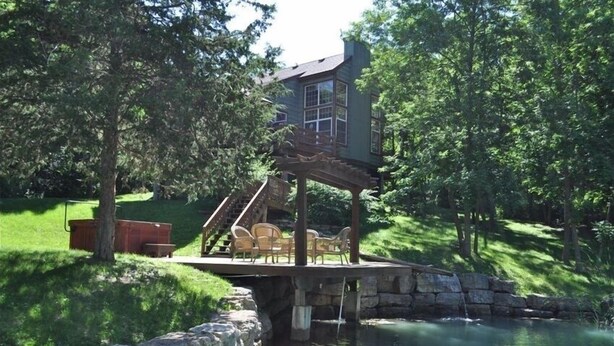 Ein Haus mit einer Terrasse, die über einen Teich hinausragt, umgeben von Bäumen.