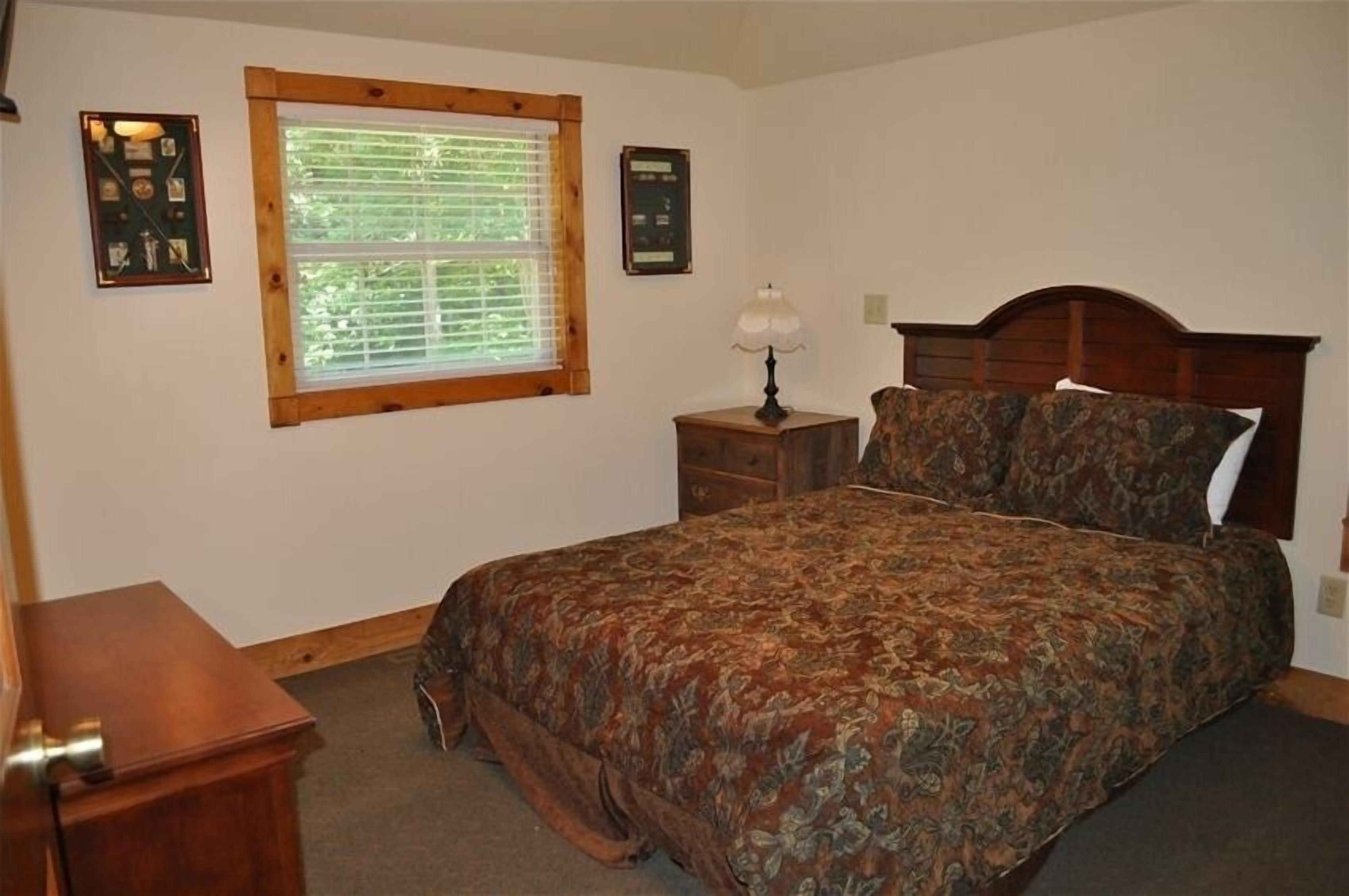 Un dormitorio con una cama de madera, una mesita de noche con lámpara, un aparador y una ventana con persianas.