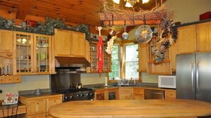 Eine Küche mit Holzausstattung, einer zentralen Kochinsel mit Barhocker, einem Herd und hängenden Dekorationen.