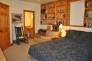 A bedroom with a bed, a chair, a sofa, a bookshelf, and a fireplace.