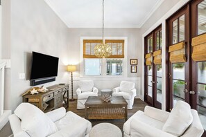 Un salon doté d’un téléviseur à écran plat, de canapés blancs, d’une table basse et d’une grande fenêtre offrant une vue dégagée.