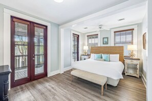 Quarto com cama grande, piso de madeira, um banco, duas mesas de cabeceira com luminárias e um ventilador de teto.
