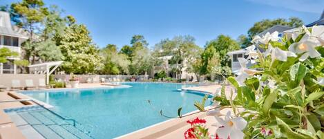 A swimming pool with clear blue water, surrounded by greenery and lounge chairs.