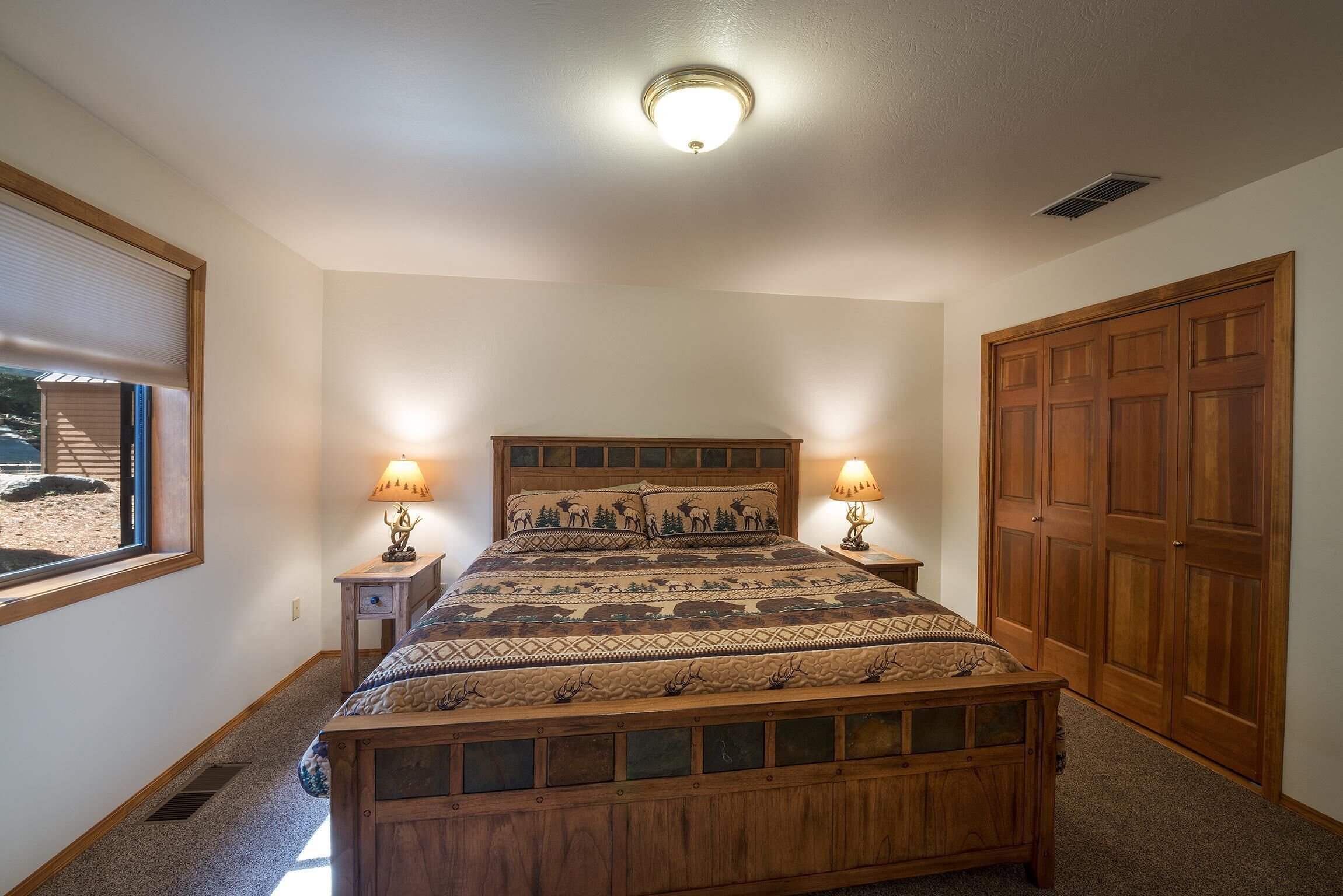 A bedroom with a wooden bed, two bedside lamps, a window with blinds, and a wooden wardrobe.