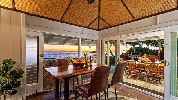 Comedor con vista al océano, una mesa de madera, sillas y una parrilla afuera.