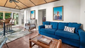 Un salón amplio con un sofá azul, una mesa de centro de madera y una zona de comedor con mesa y sillas.