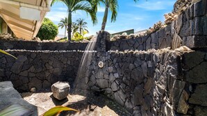 Una fuente de piedra con una cascada, rodeada de palmeras y un muro de piedra.