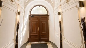 Ein Korridor mit gewölbter Decke, dekorativen Blumenmustern, einer zweiflügeligen Holztür und Wandleuchtern.