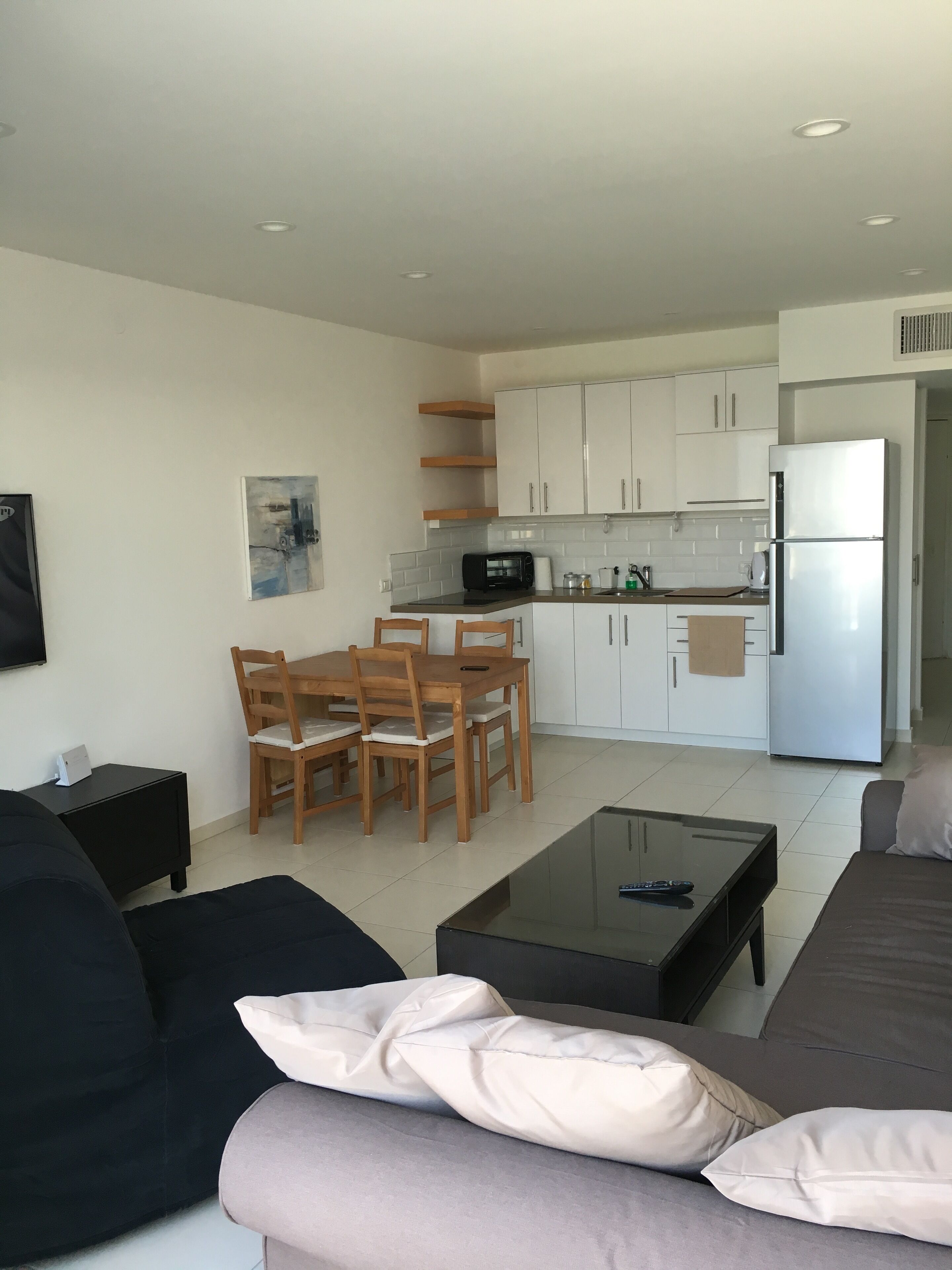 A modern living room with a sofa, a glass coffee table, and a dining area with wooden chairs and a small table.