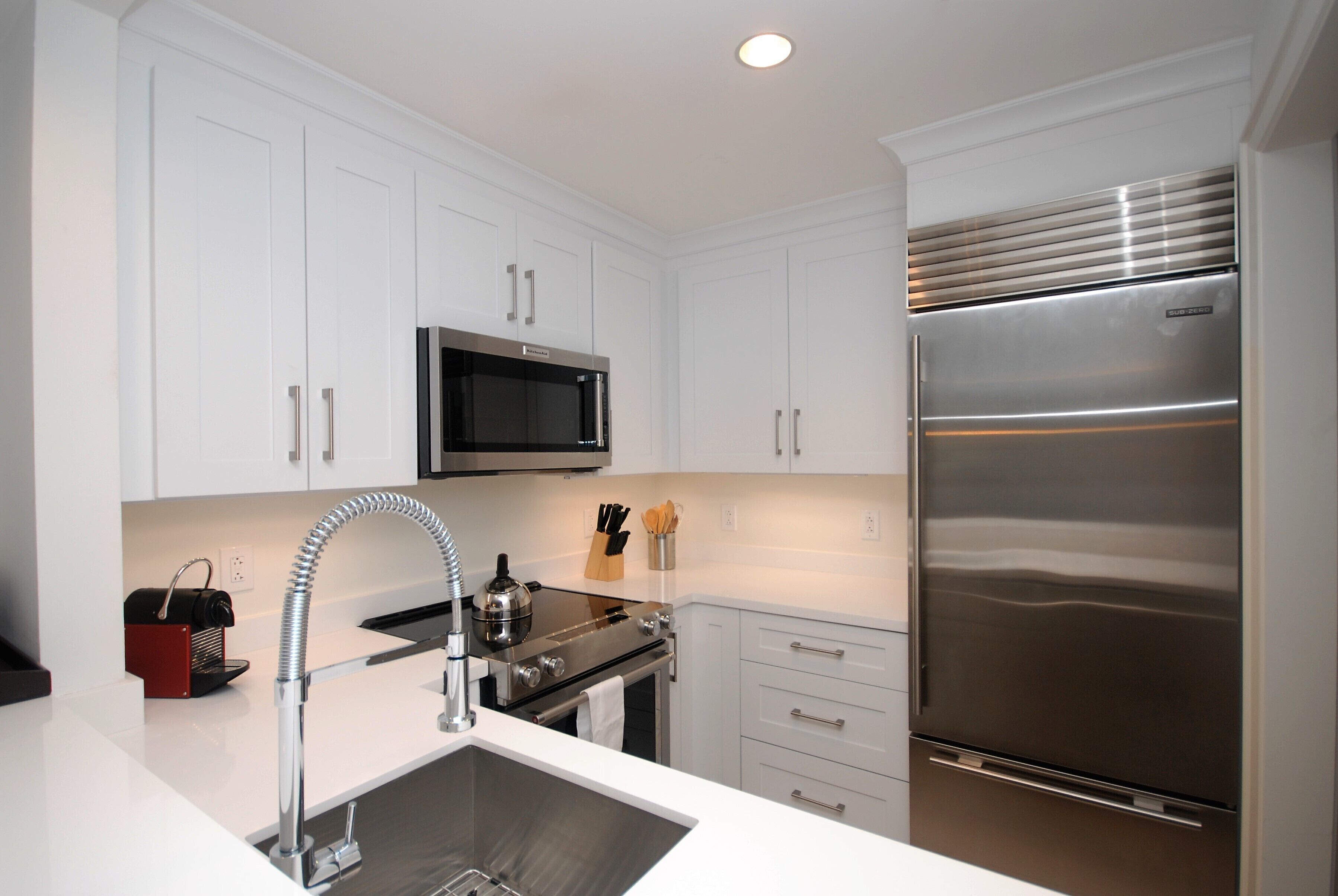 A modern kitchen with white cabinets, stainless steel appliances, and a built-in oven.