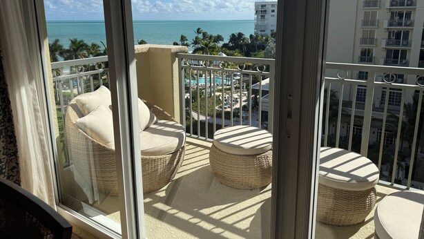 Een balkon met rieten meubilair en uitzicht op zee en het zwembad van het resort.