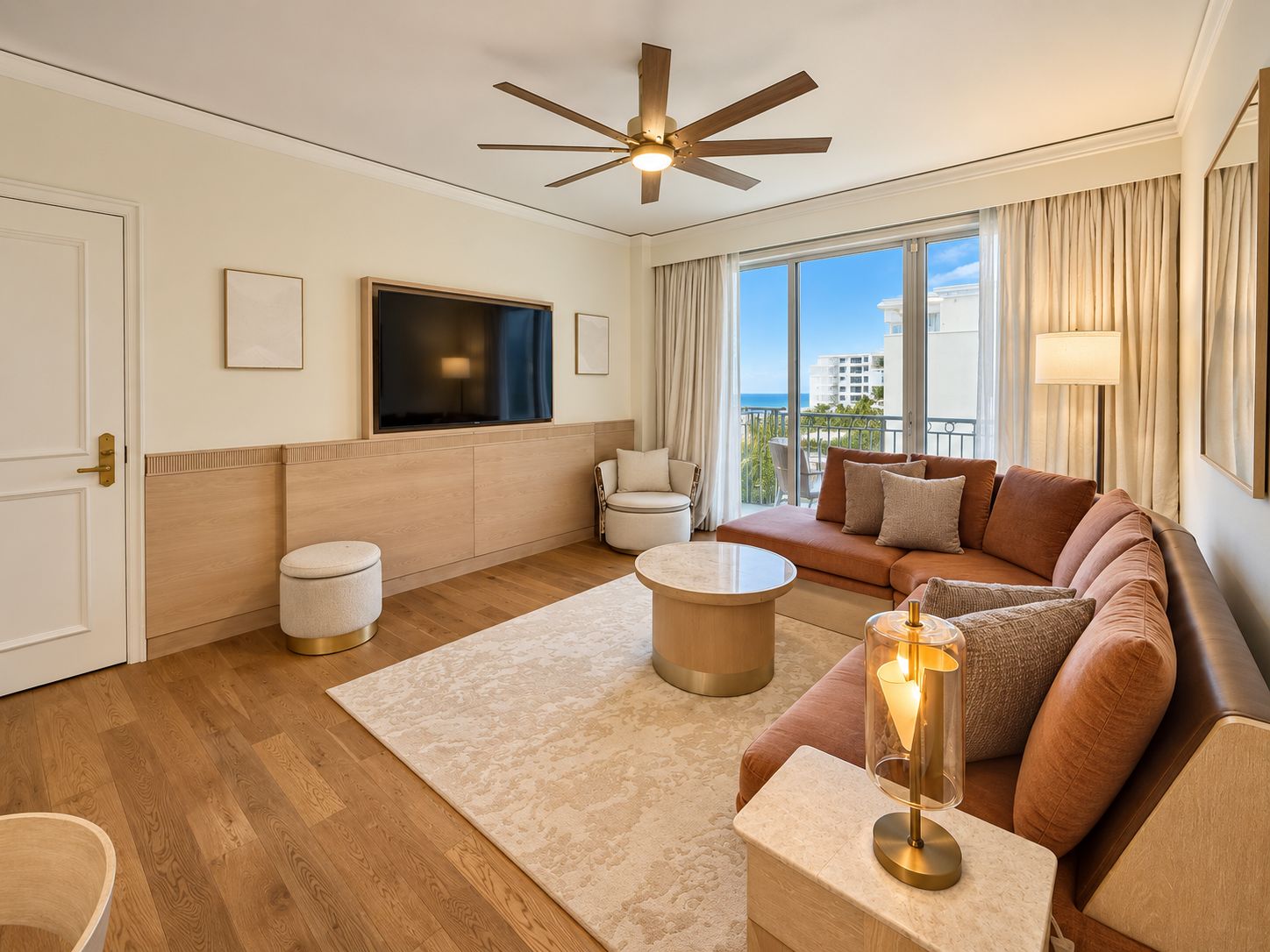 Une chambre d’hôtel moderne dotée d’une grande fenêtre, d’un ventilateur de plafond, d’un téléviseur à écran plat, d’un canapé, d’une table basse et d’une lampe.
