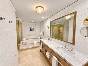 A bathroom with a large mirror, two sinks, a bathtub, and a shower.