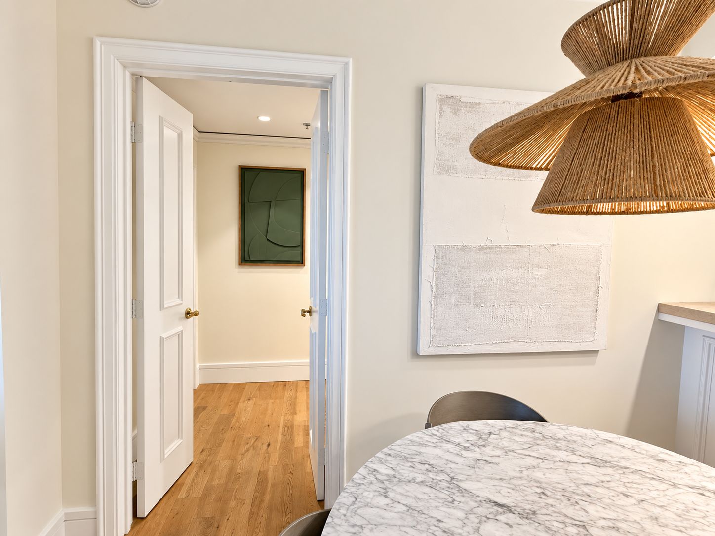 A room with a marble table, a wicker pendant light, and a door leading to another room.