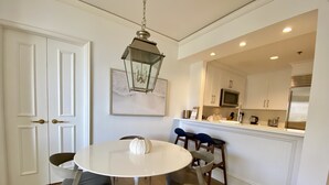Een eetruimte met een ronde tafel, vier stoelen, een hanglamp en een keuken op de achtergrond.