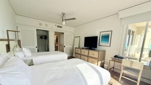 Een hotelkamer met twee bedden, een bureau met een computer, een televisie en een raam met uitzicht op zee.