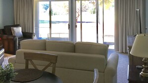 Una sala de estar con sofá, mesa de centro y lámpara. Se ve un cuerpo de agua a través de las ventanas.