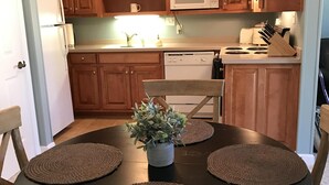 Una cocina con armarios de madera, microondas, lavavajillas y una mesa redonda con individuales y una planta en maceta.