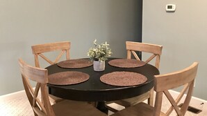 Una mesa de comedor redonda con seis sillas de madera, una planta en el centro y un detector de humo en la pared.