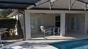 Et poolområde med liggestole, en overdækket terrasse og udsigt til poolen.