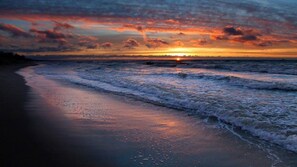 A beach at sunset with waves approaching the shore.