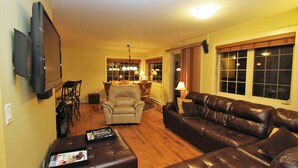 A living room with a brown leather sofa, a beige armchair, and a TV mounted on the wall. - Spectacular Top Floor 2 Br W/ Hot Tub and Panoramic View (Golden)