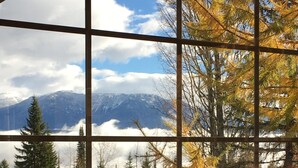 A room with a large window offering a view of a mountainous landscape and autumn foliage. - Spectacular Top Floor 2 Br W/ Hot Tub and Panoramic View (Golden)