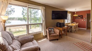 A living room with a sofa, armchair, dining table, chairs, a TV, and a view of a lake. - Private Lodge on Private Lake, Embarrass MN. Boat & Motor Cable WiFi Internet  (Embarrass)