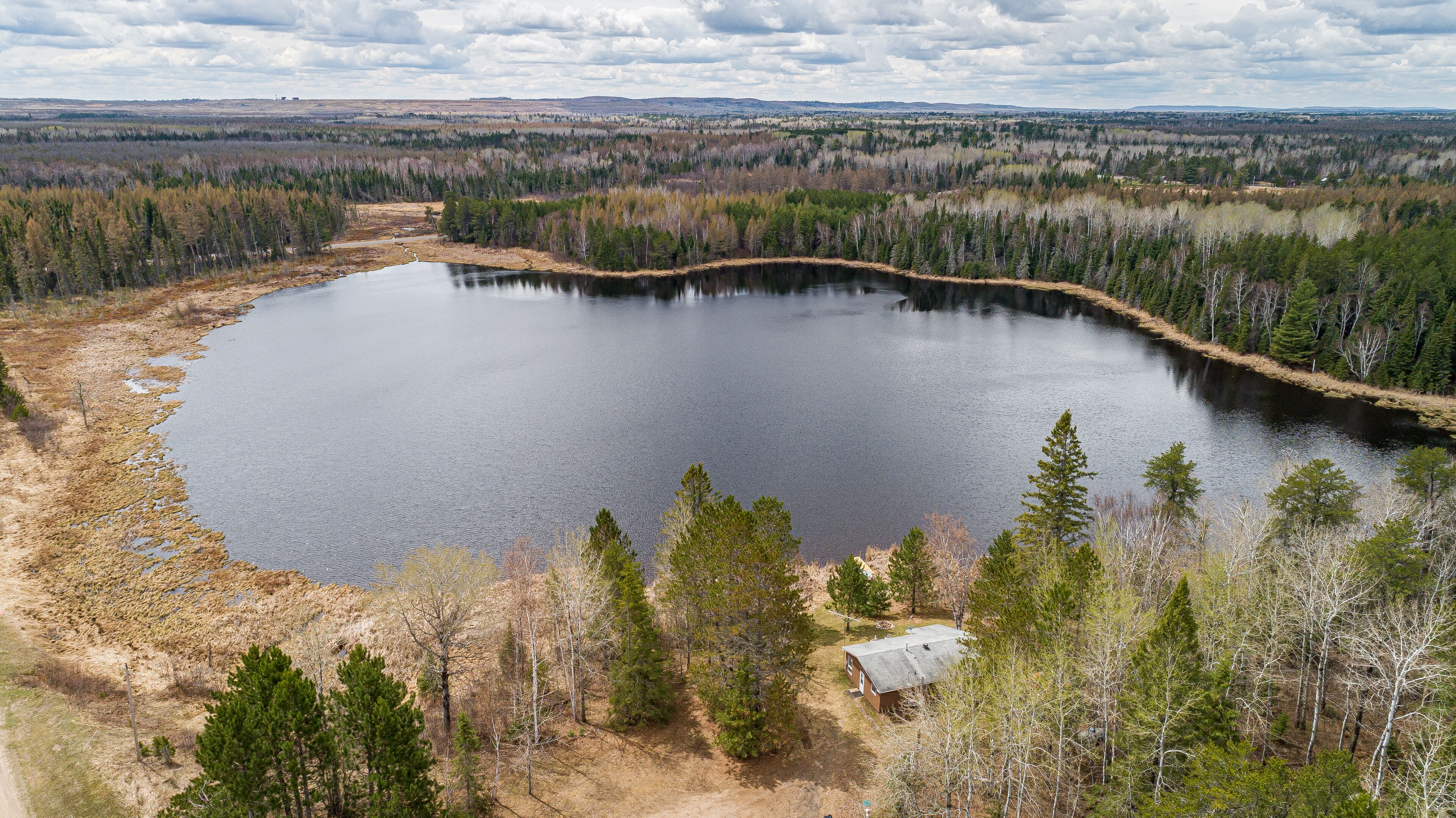 Un lago amplio y tranquilo rodeado de un bosque denso y una cabaña pequeña.