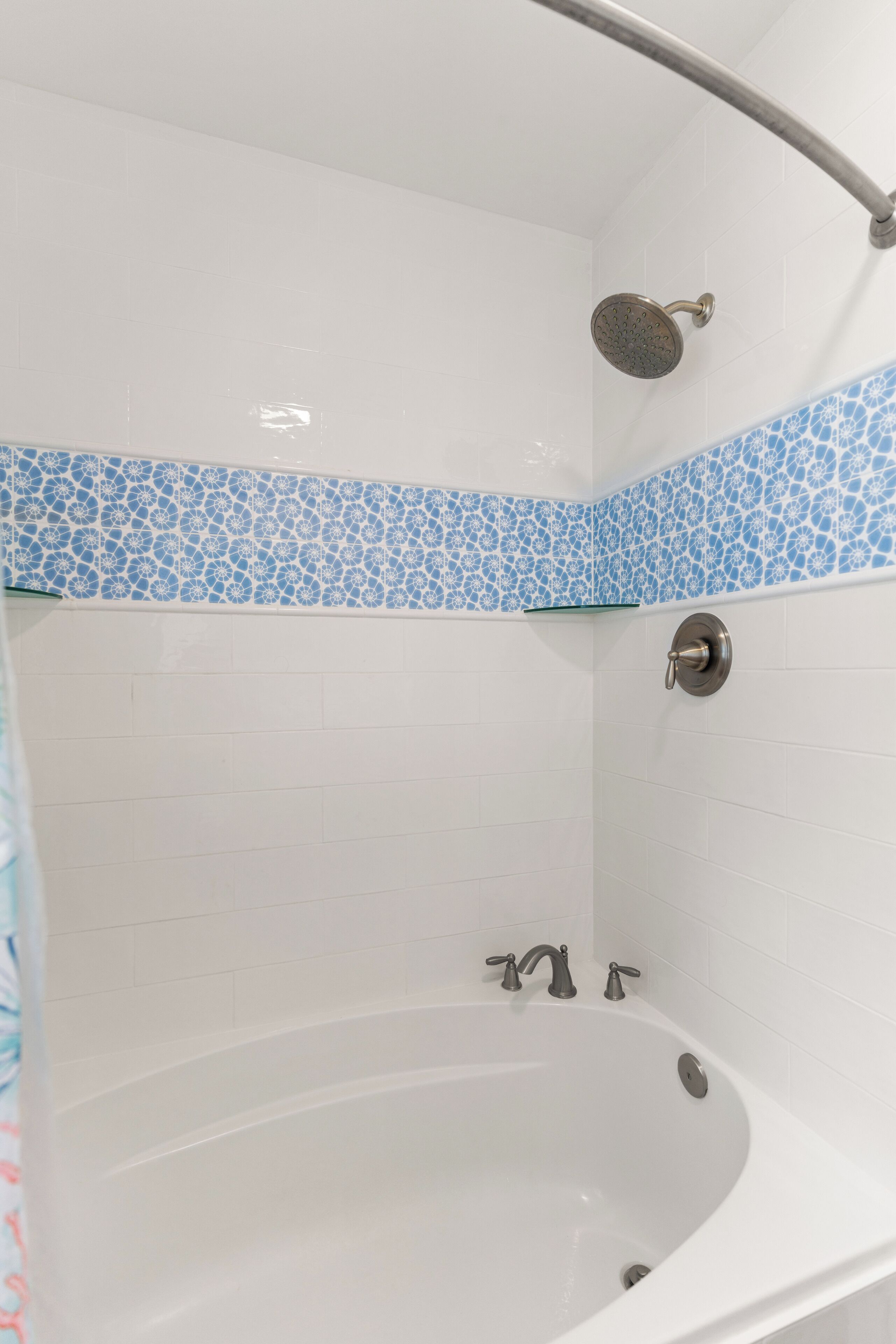 A bathroom with a bathtub, a showerhead, and a glass shelf.