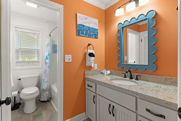 A bathroom with a white toilet, a sink with a blue mirror, and an orange wall.