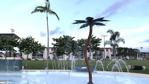 A public fountain with multiple water jets, surrounded by palm trees and a grassy area. - Beautiful Condo at Madeira Beach, 2Htd Pools,Walk to Beach,WiFi,Piers,Johns Pass (Madeira Beach)