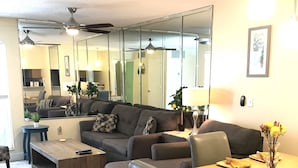 A modern living room with a sofa, a dining table, and a coffee table. There is a mirror on the wall and a ceiling fan. - Beautiful Condo at Madeira Beach, 2Htd Pools,Walk to Beach,WiFi,Piers,Johns Pass (Madeira Beach)