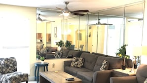 A living room with a sofa, armchair, coffee table, and a large mirror reflecting the room. - Beautiful Condo at Madeira Beach, 2Htd Pools,Walk to Beach,WiFi,Piers,Johns Pass (Madeira Beach)
