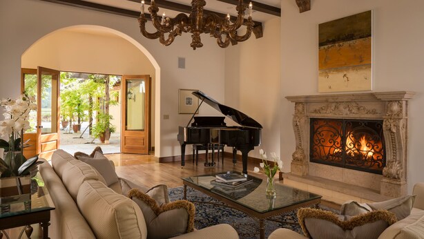 A spacious living room with a grand piano, a fireplace, and a chandelier. - Luxury Napa Valley Estate Surrounded by Vineyards (Calistoga)