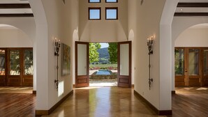 A spacious hallway with a pool view, wooden floors, and multiple doors. - Luxury Napa Valley Estate Surrounded by Vineyards (Calistoga)