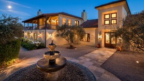 A two-story house with a courtyard, a fountain, and a well-lit entrance. - Luxury Napa Valley Estate Surrounded by Vineyards (Calistoga)