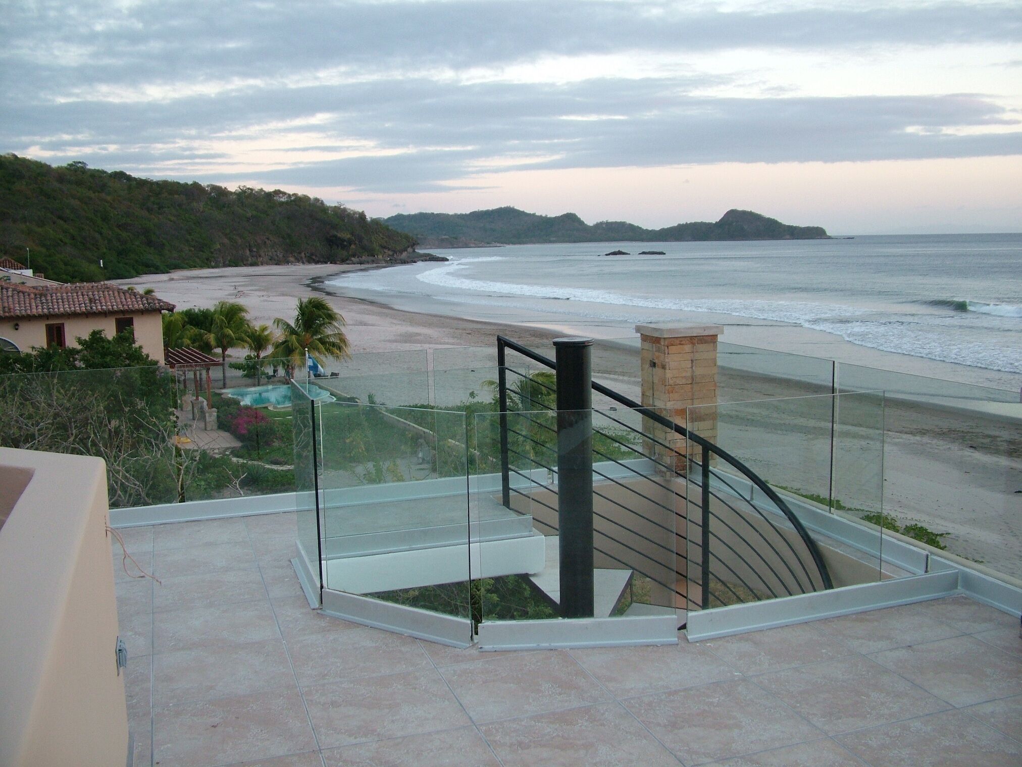 A balcony with a glass railing overlooking a beach and ocean.