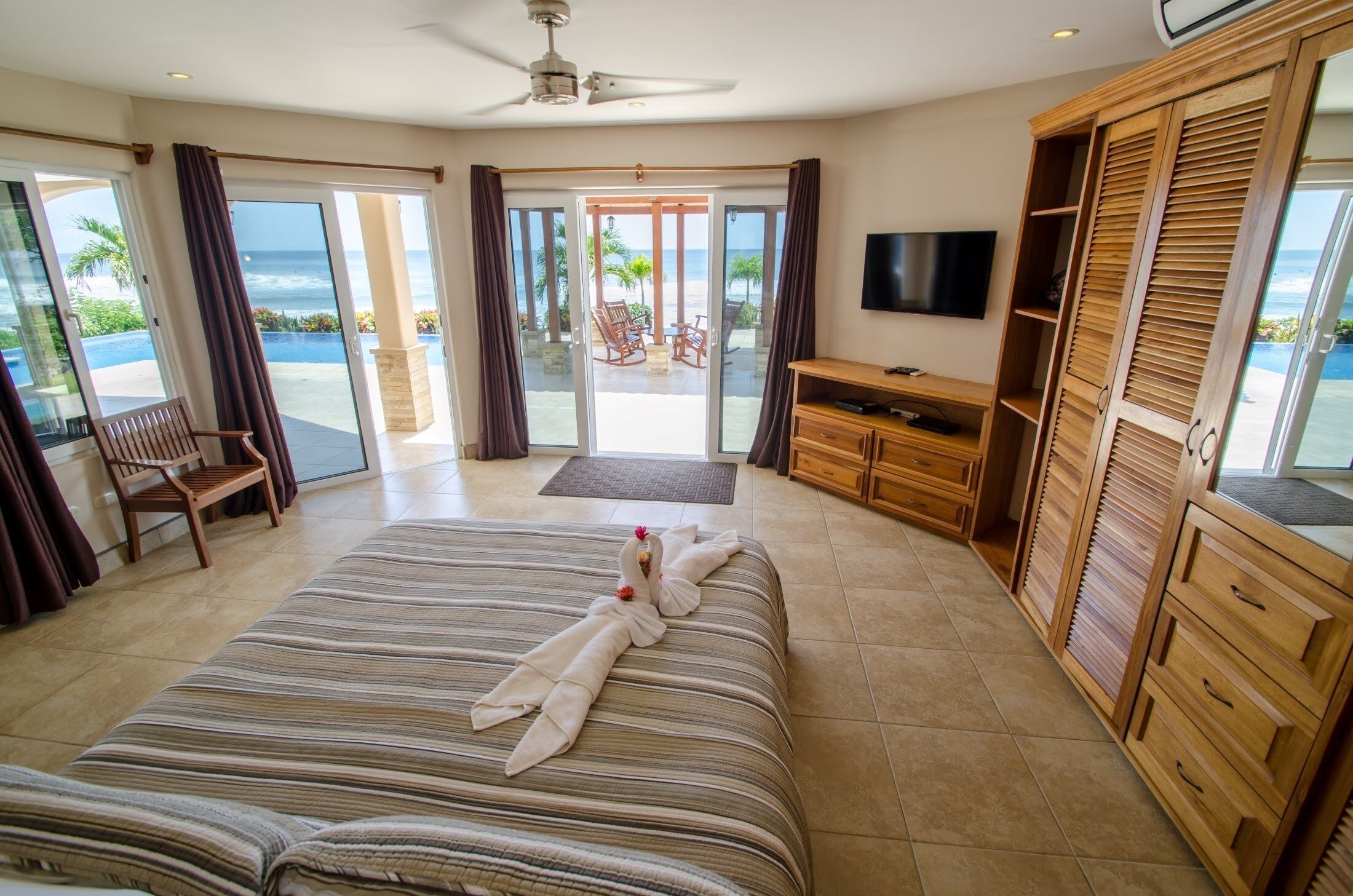 Habitación de hotel con una cama grande, televisor, muebles de madera y vista al océano.