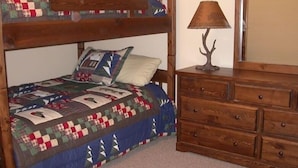 Un lit superposé avec une courtepointe, une commode avec des tiroirs et une lampe décorée d’un motif d’arbre.