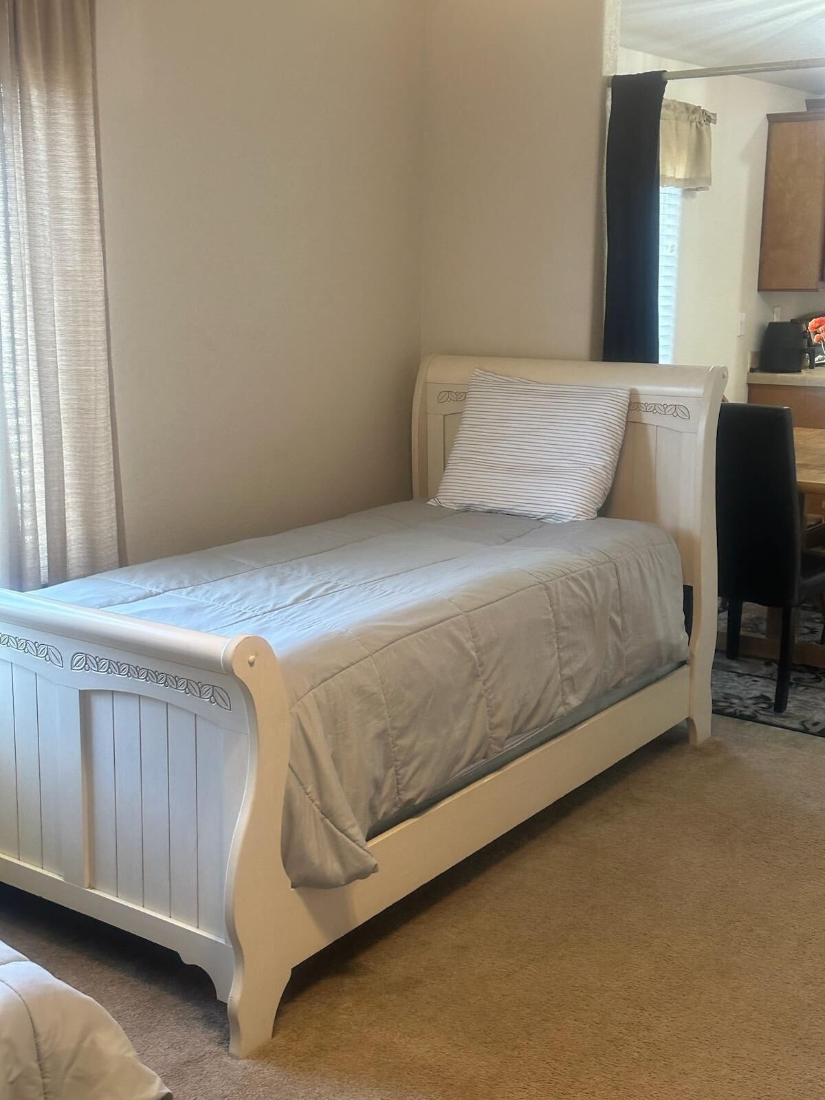 A single bed with a headboard, a bedside table, and a chair in a room with a carpeted floor.